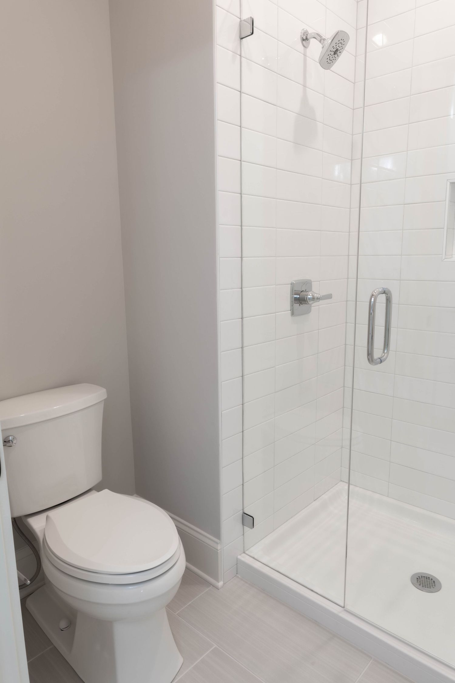 Modern bathroom with glass shower enclosure, white tile, and toilet.