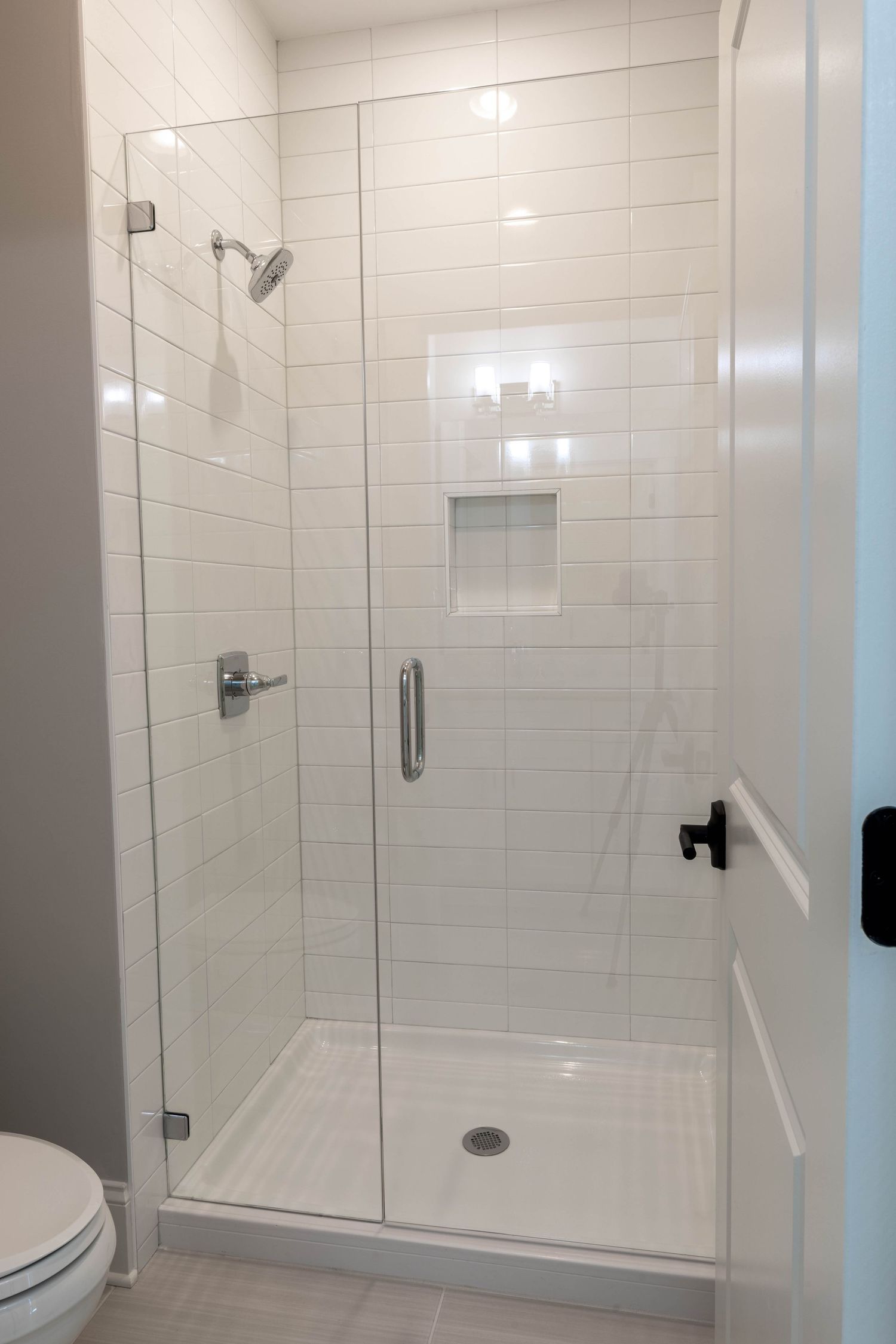 Glass-enclosed shower with white subway tile, built-in niche, and chrome fixtures.
