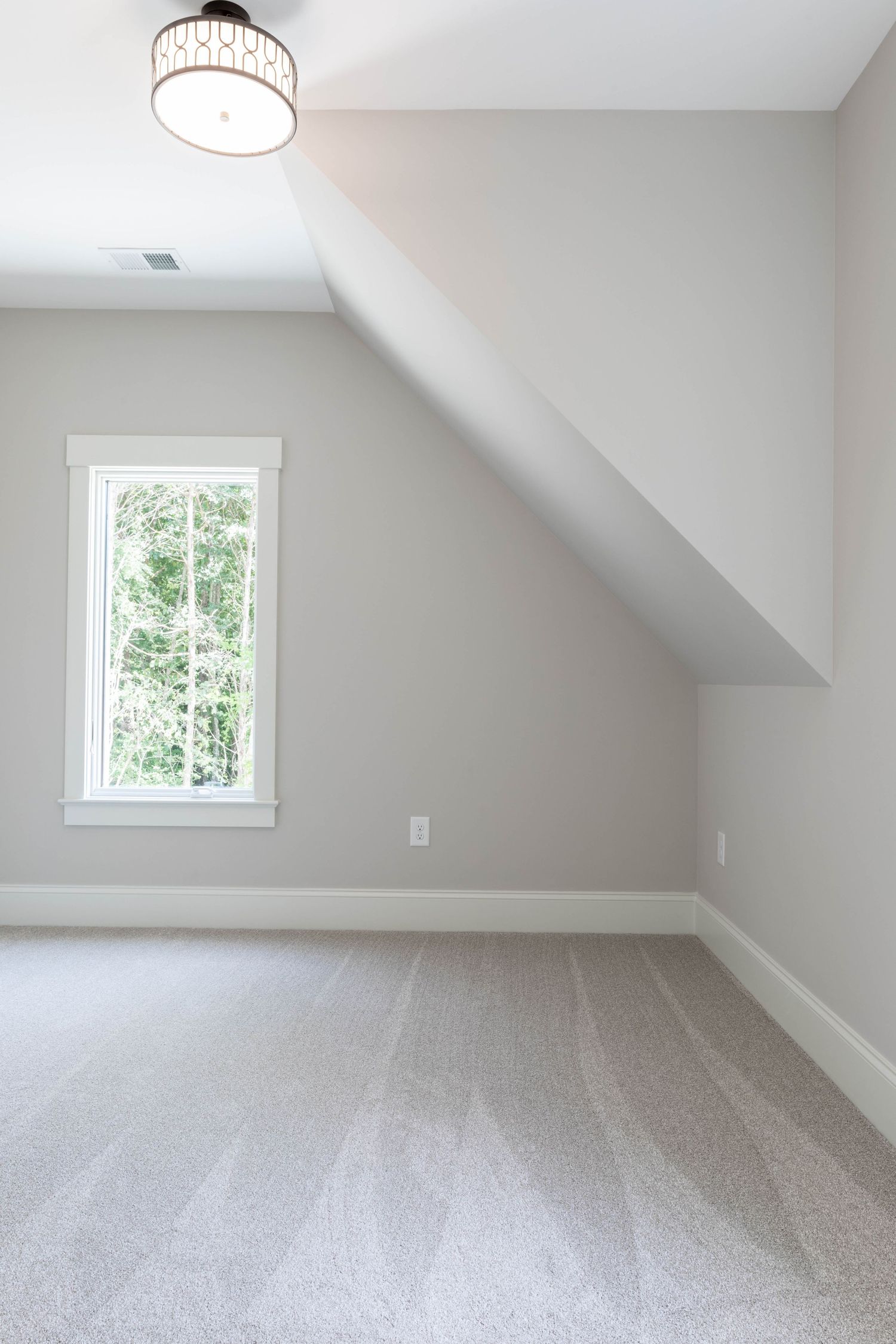 Carpeted room with sloped ceiling, contemporary light fixture, and tall window providing natural light.