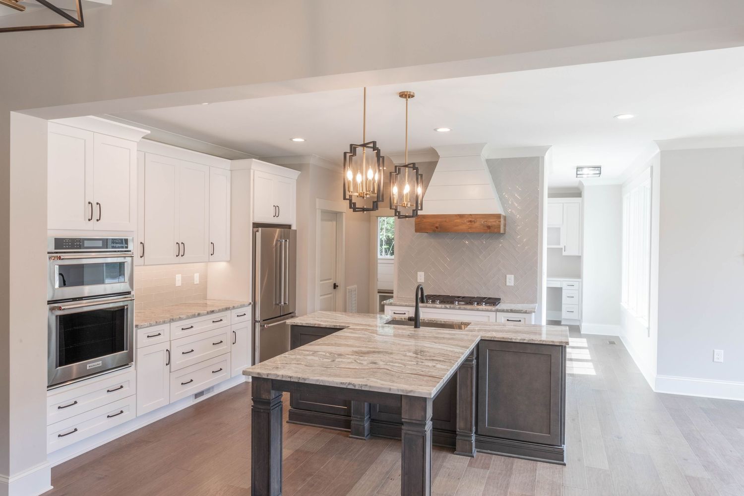 Modern kitchen design with white cabinets, grey island, marble countertops and pendant lighting fixtures.
