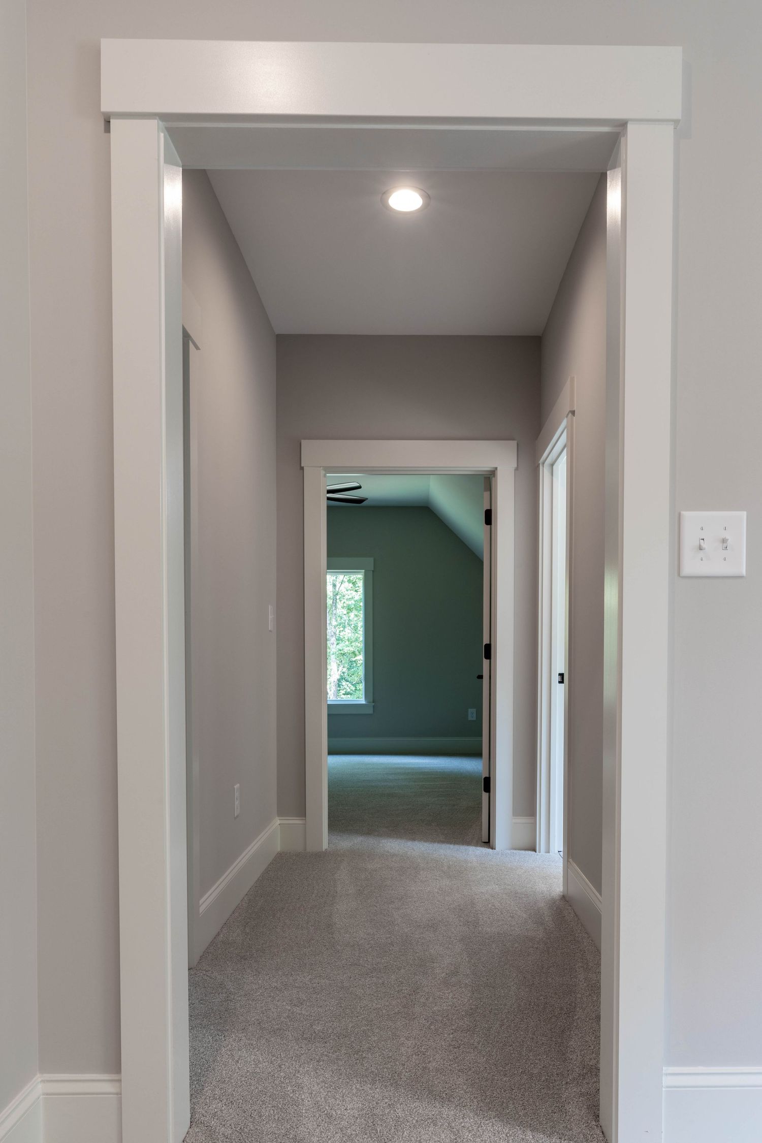 Long hallway with grey walls, white trim and carpeted flooring leading to rooms with natural light.