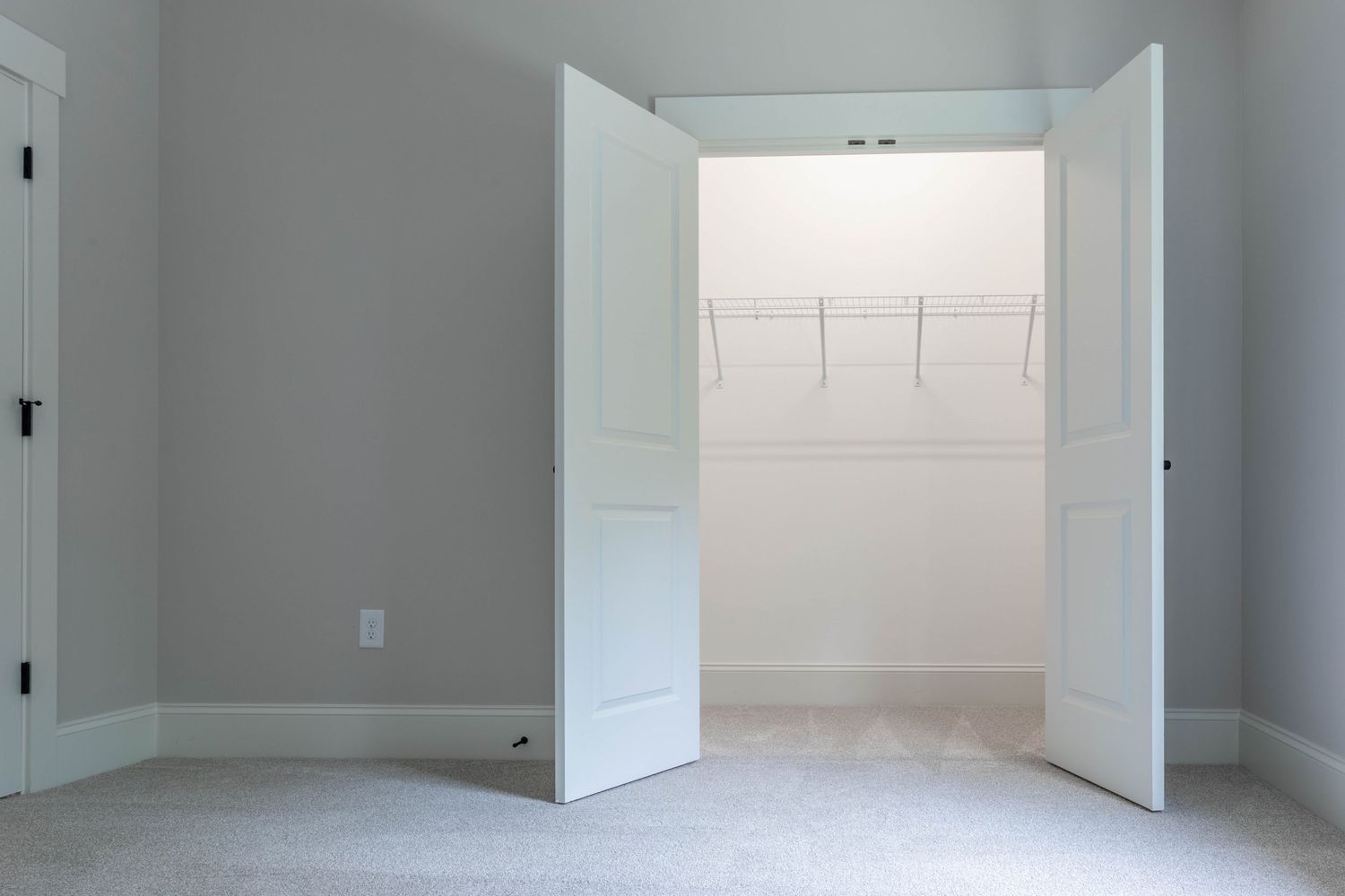 Walk-in closet with white double doors and wire shelving system against light grey walls.