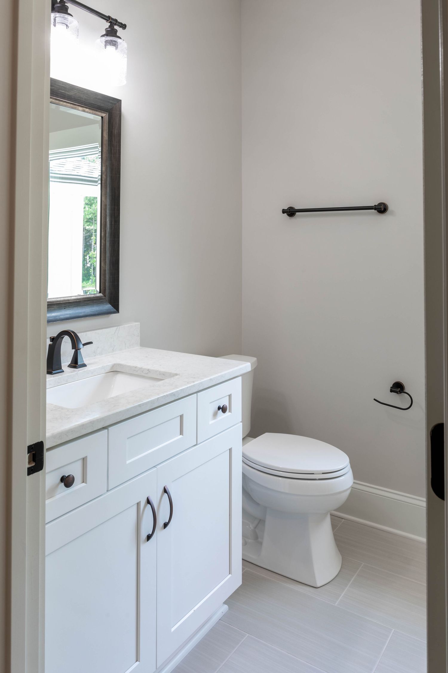Minimalist bathroom featuring white vanity, black accents, and light grey tile flooring.