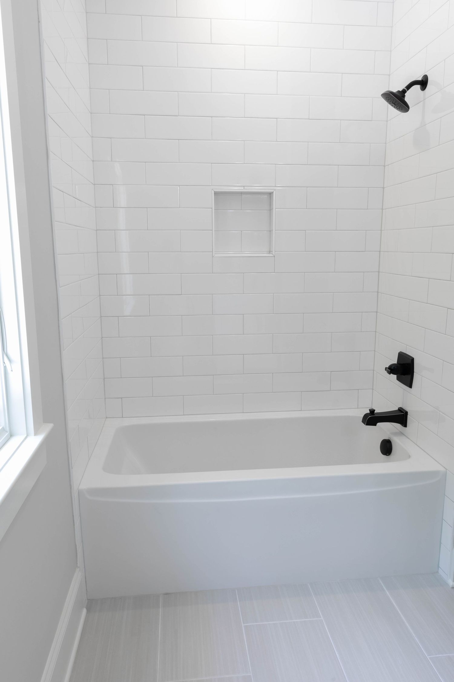 White subway tiled bathroom with built-in tub, shower niche, and matte black fixtures.