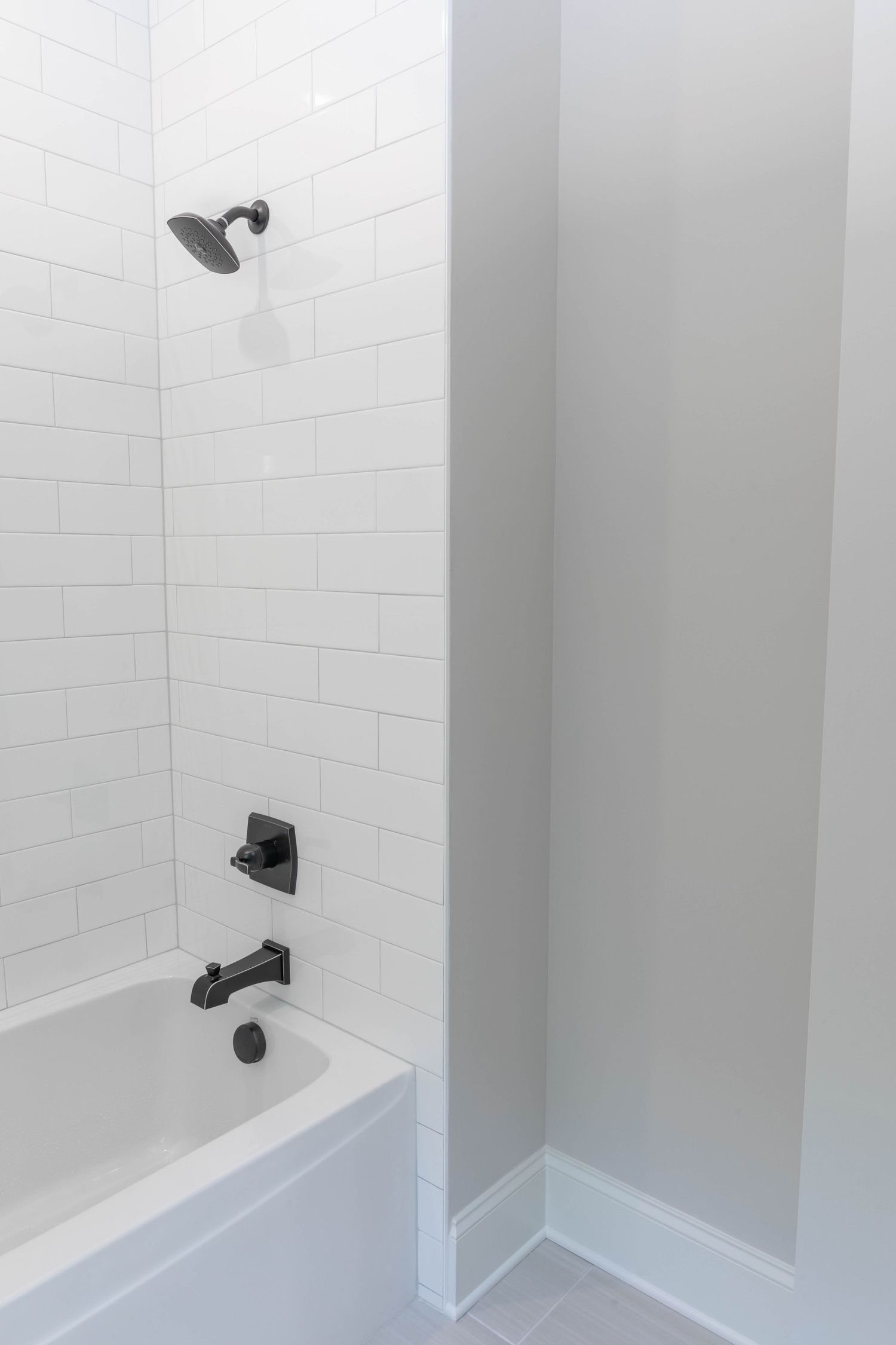 Modern white bathtub with subway tile surround and matte black plumbing fixtures.