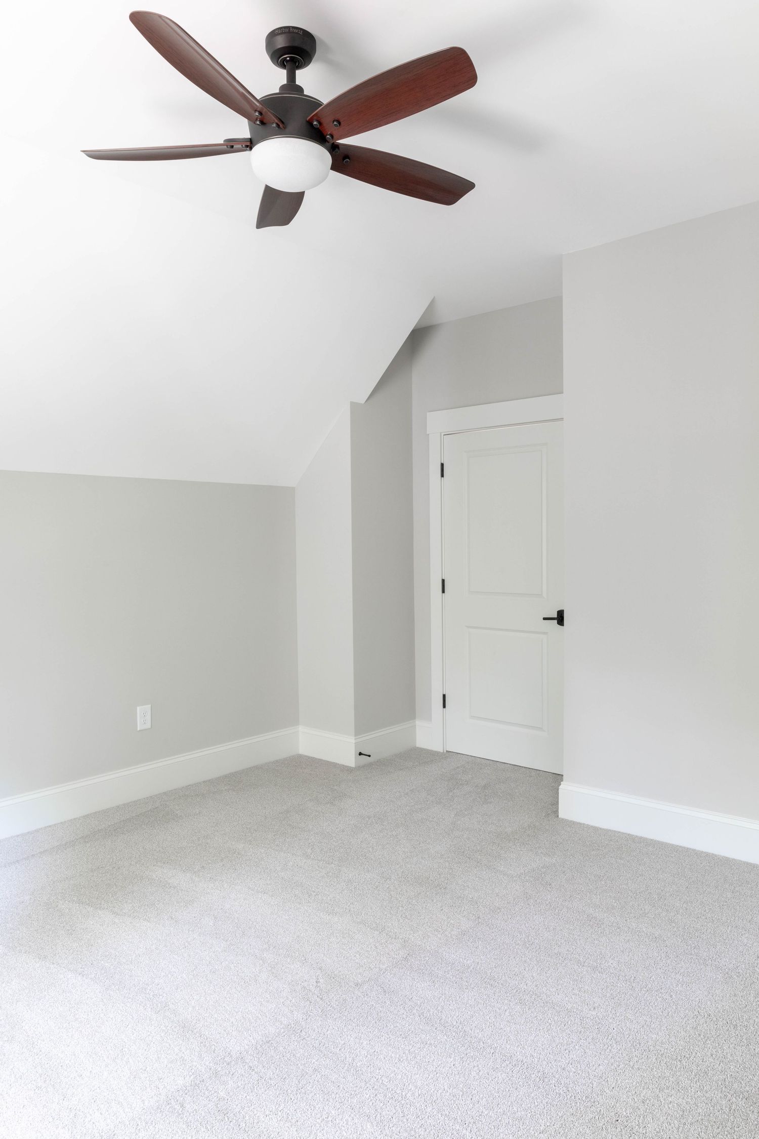 Empty bedroom with vaulted ceiling, ceiling fan, and grey walls on carpet flooring.