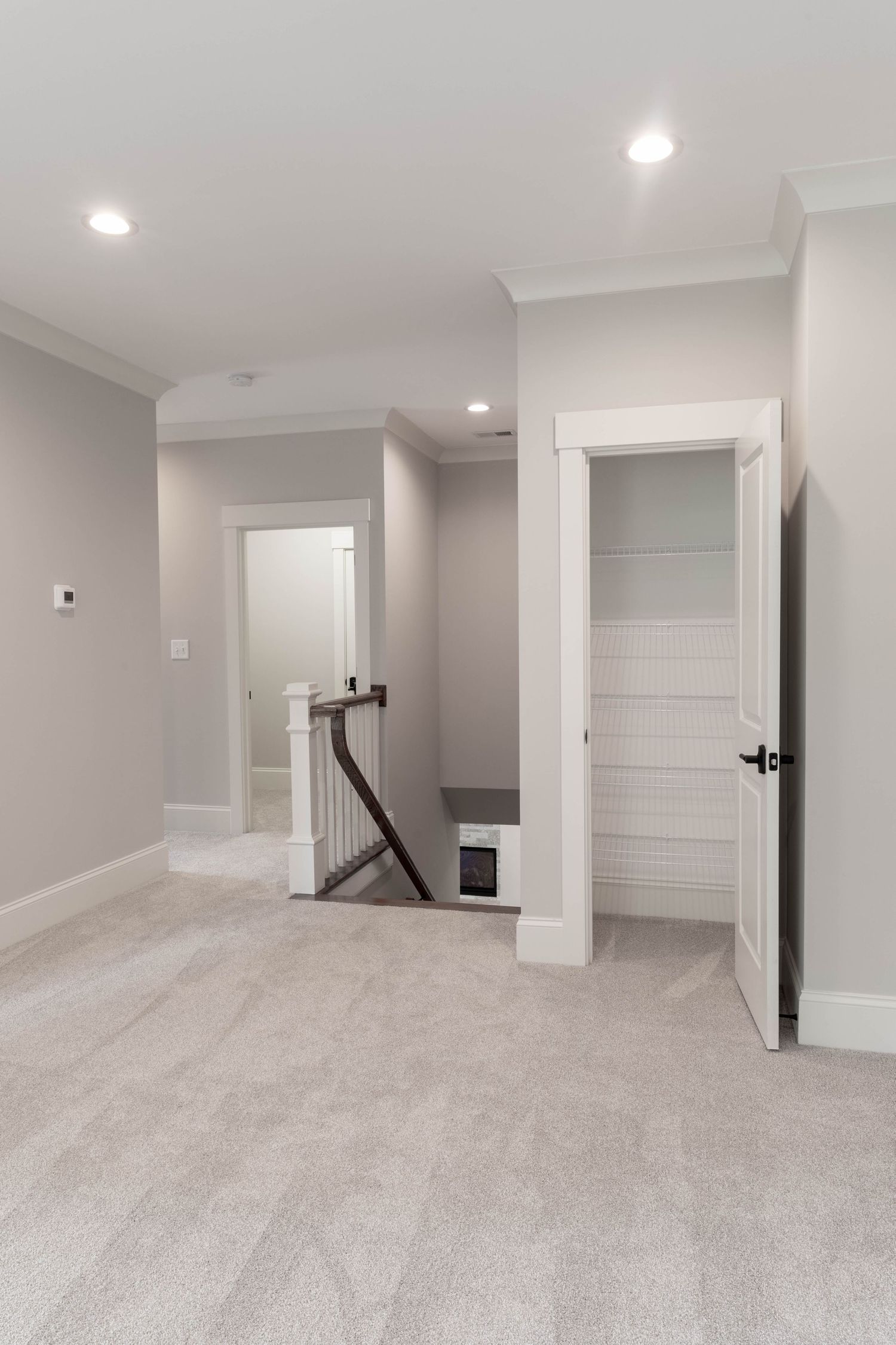 Modern hallway with gray walls, white doors, and beige carpet leading to a staircase with recessed lighting.