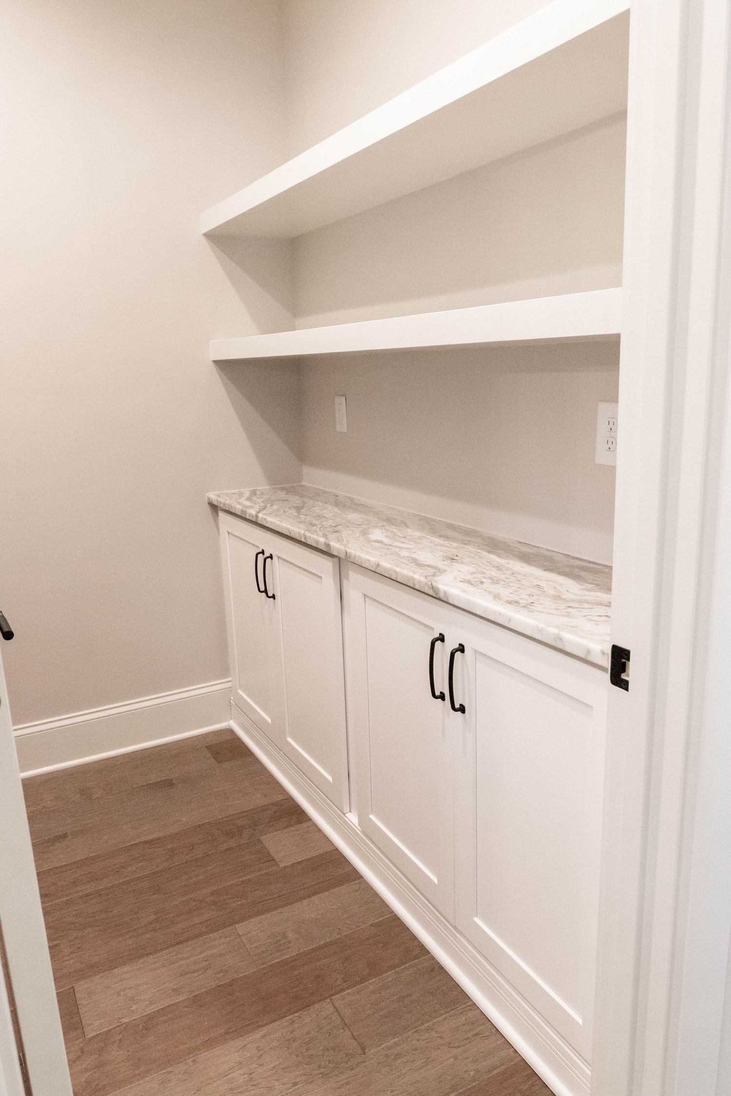 Built-in white cabinets with marble countertop and floating shelves in a modern storage space.