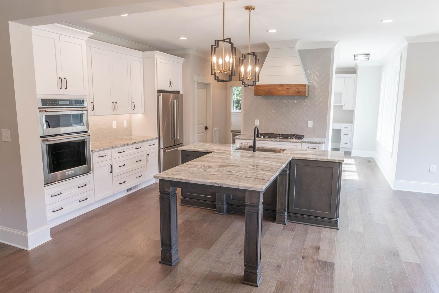 Spacious kitchen featuring white cabinetry, stainless appliances, grey island and marble countertops with pendant lights.
