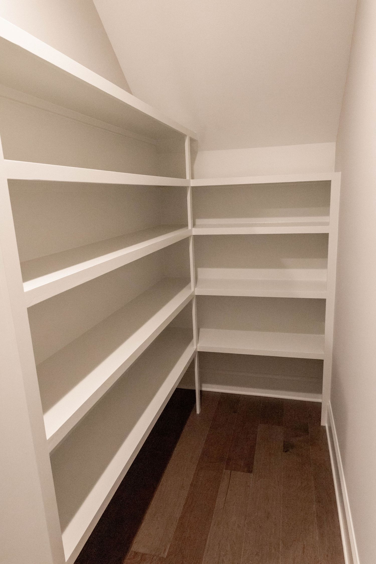 Walk-in pantry with multiple white shelves and hardwood flooring.