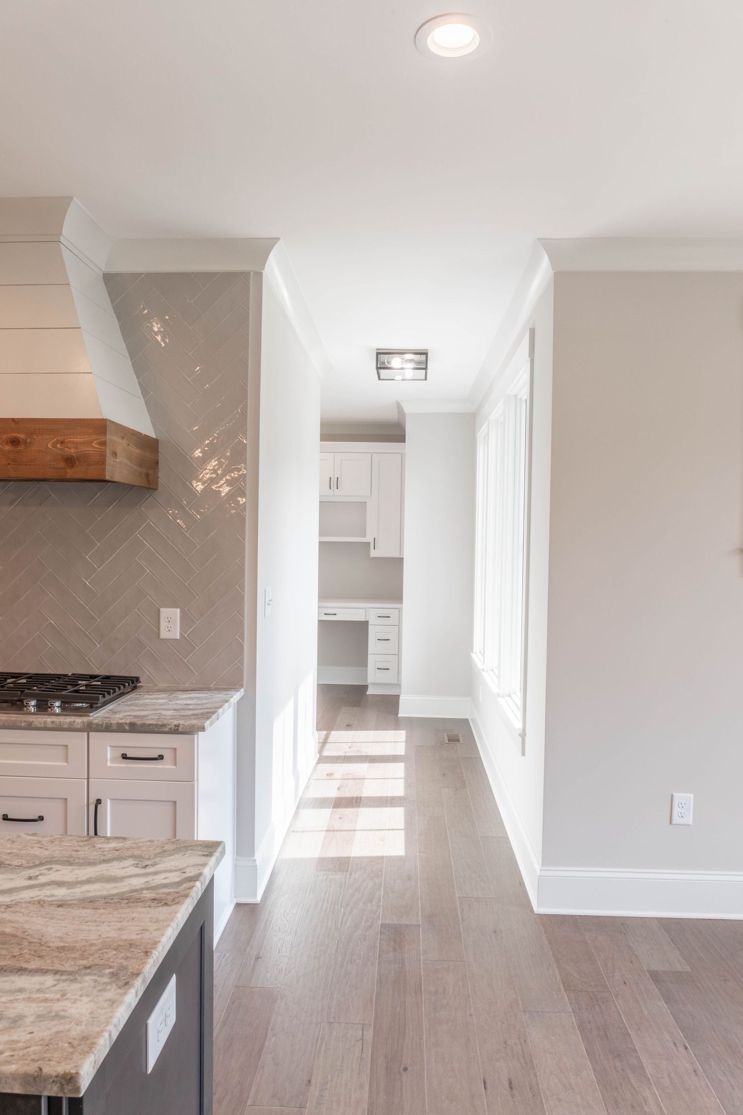 Bright hallway with white kitchen cabinets, marble countertops, and light hardwood flooring.