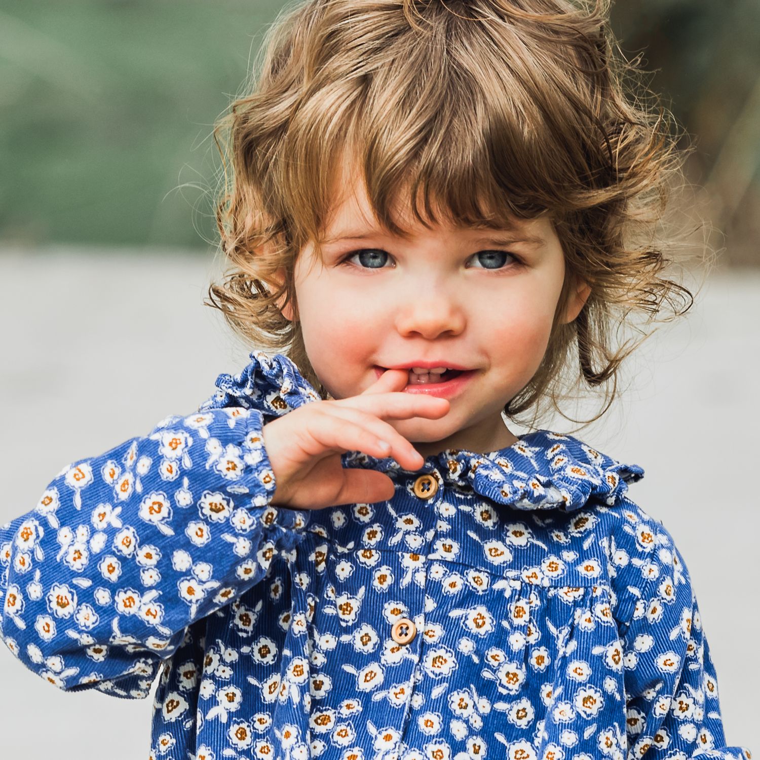 toddler girl in blue dress with one finger in mouth