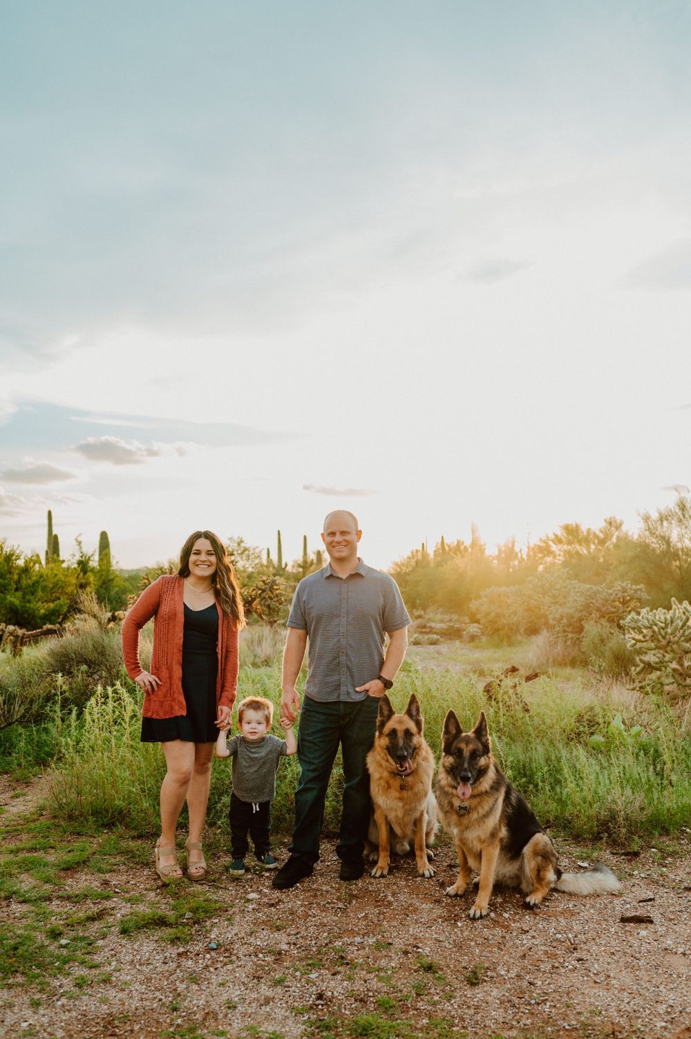 A family and their German Shepherd dogs pose together on a desert trail at sunset.