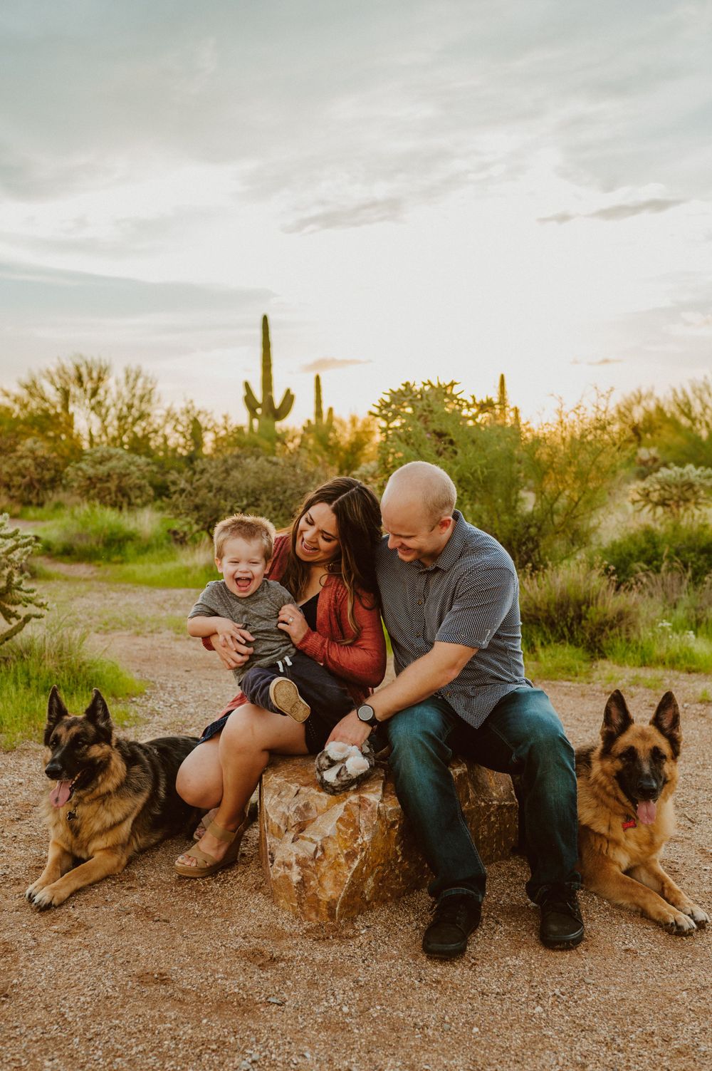 A happy family shares laughs while sitting with their German Shepherds in a desert landscape.