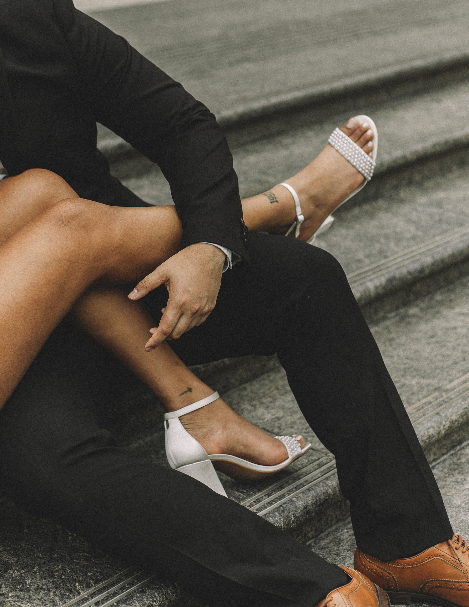 Stylish white heels and black pants detail on concrete steps with moody lighting.