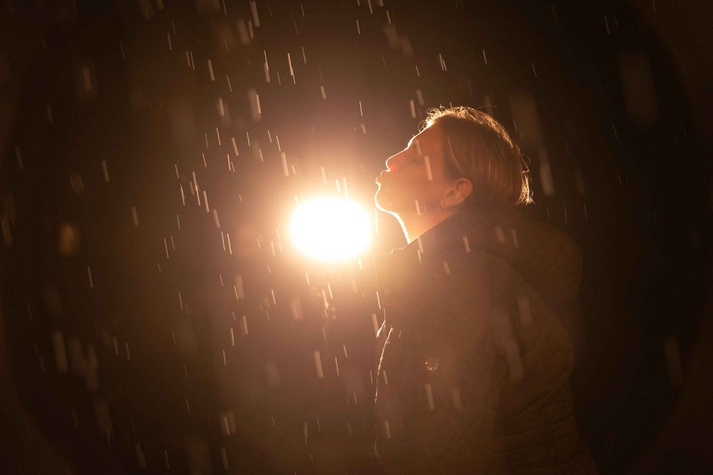 Backlit profile in dark setting with snow or rain falling around bright light source.