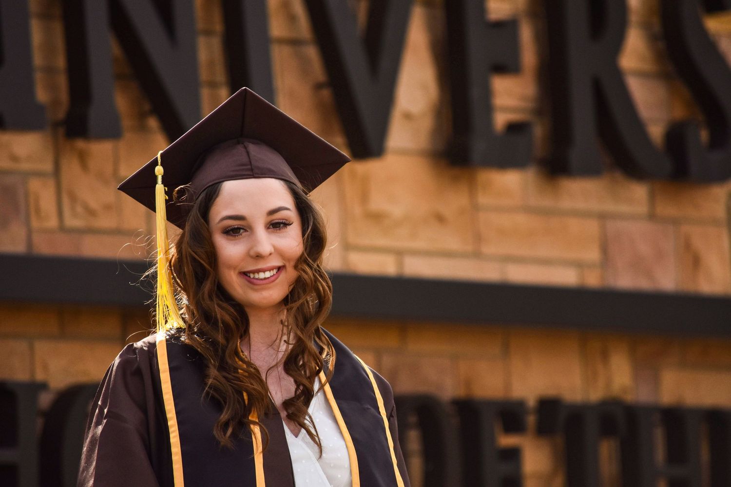 Graduate in cap and gown smiling outdoors during commencement ceremony.