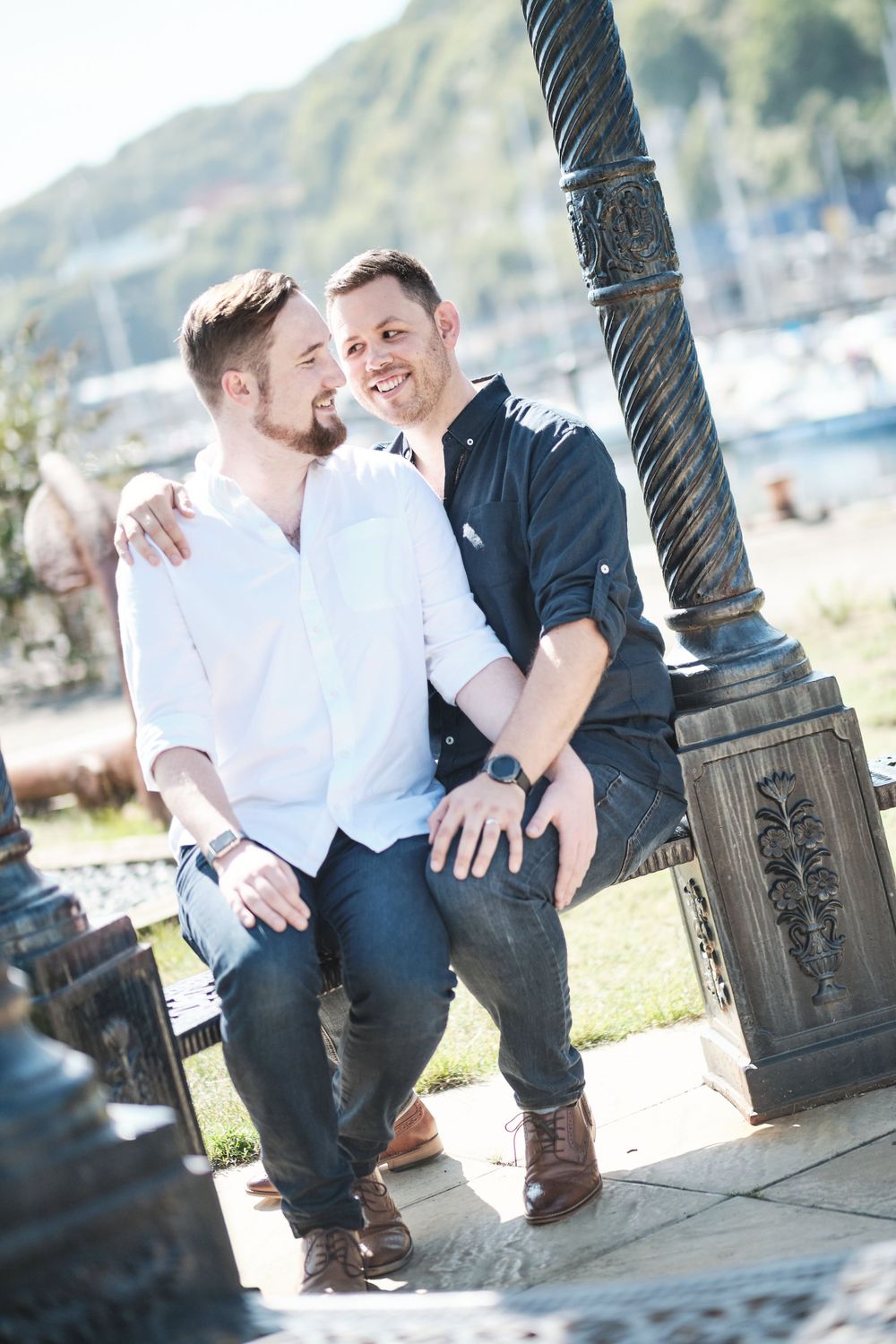 Two people in contrasting shirts share an intimate moment beside a decorative post near the marina.
