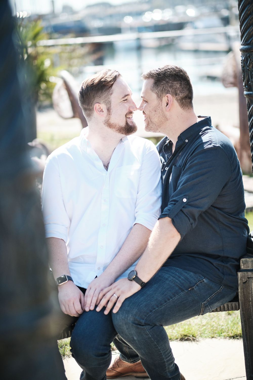 Intimate couple moment captured against marina backdrop on sunny day.