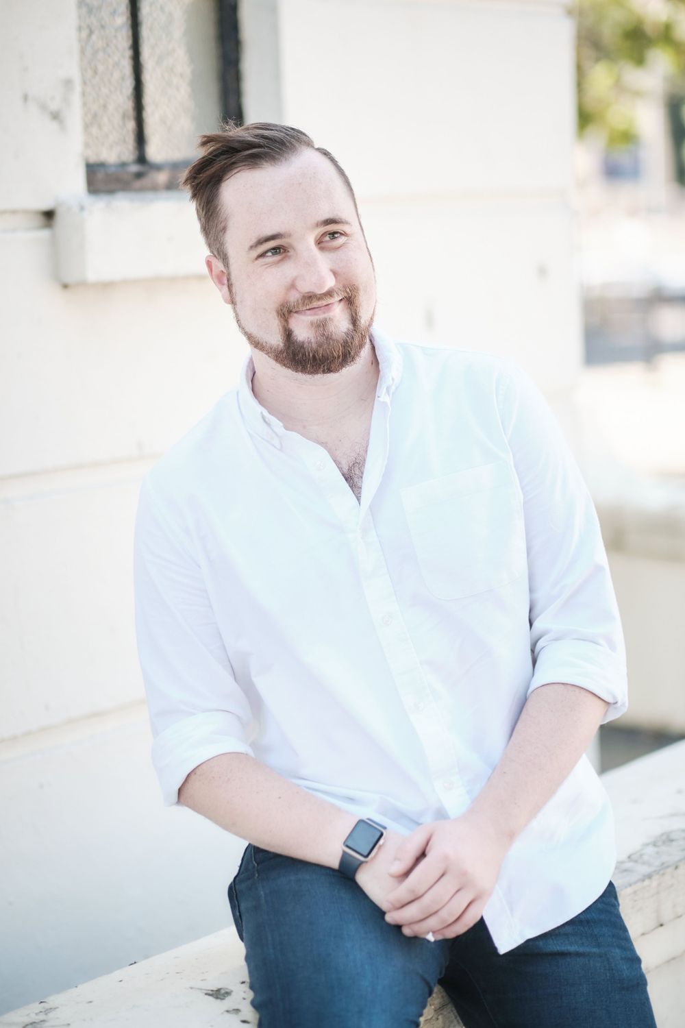 Person in white button-down shirt sits casually against white wall wearing smart watch.