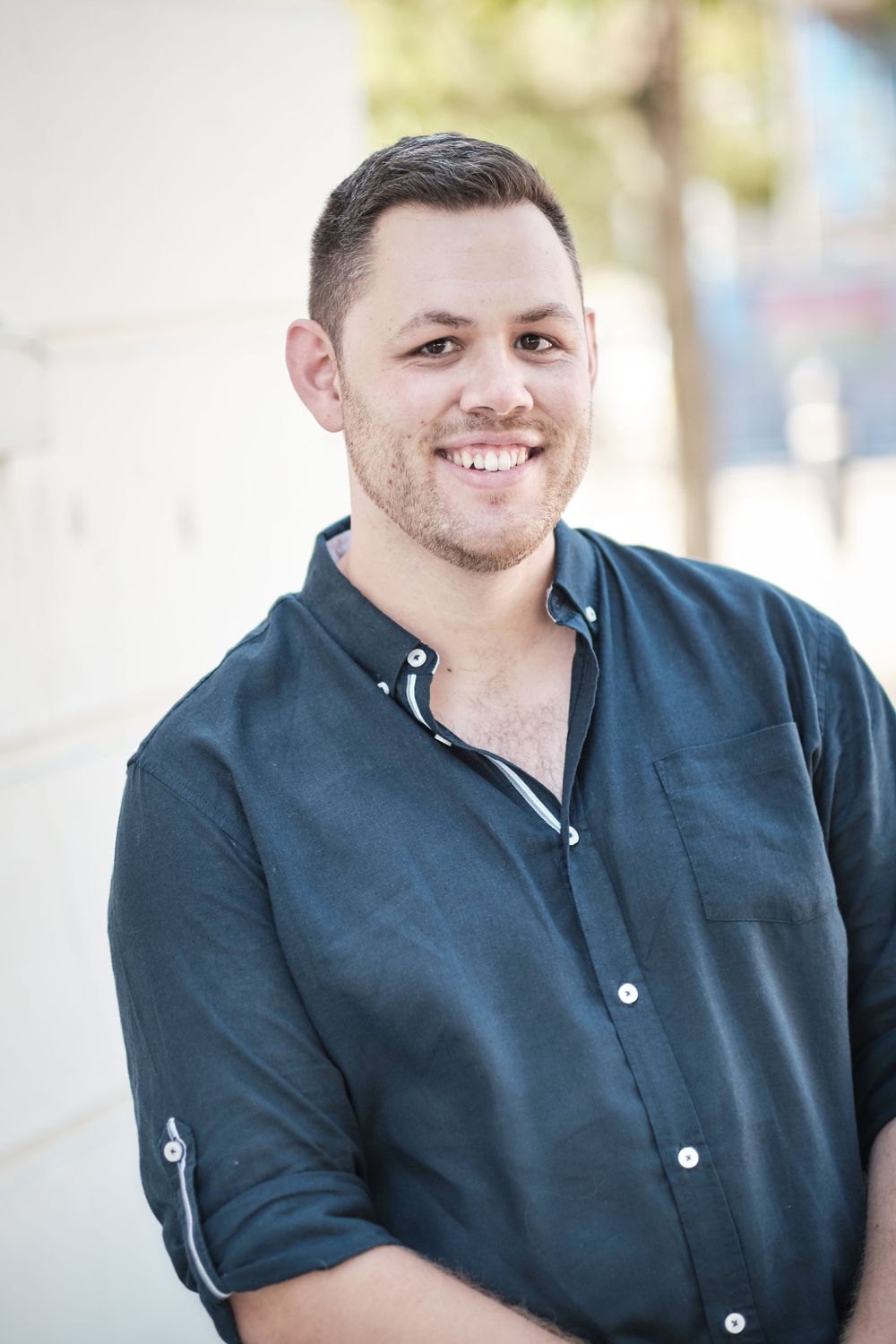 Portrait of person in dark button-down shirt smiling against blurred background.