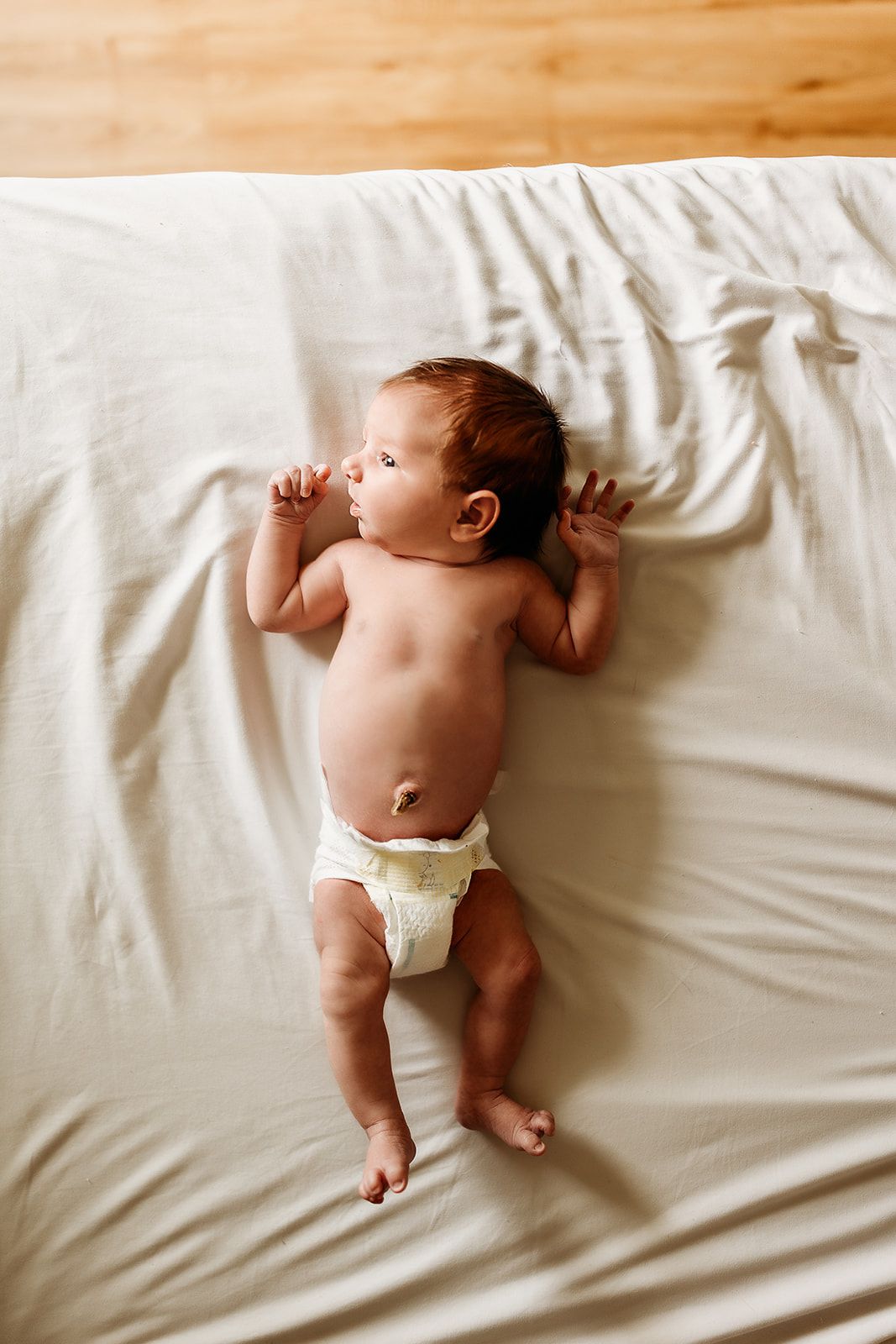A baby wearing a diaper lays on her mother's bed.