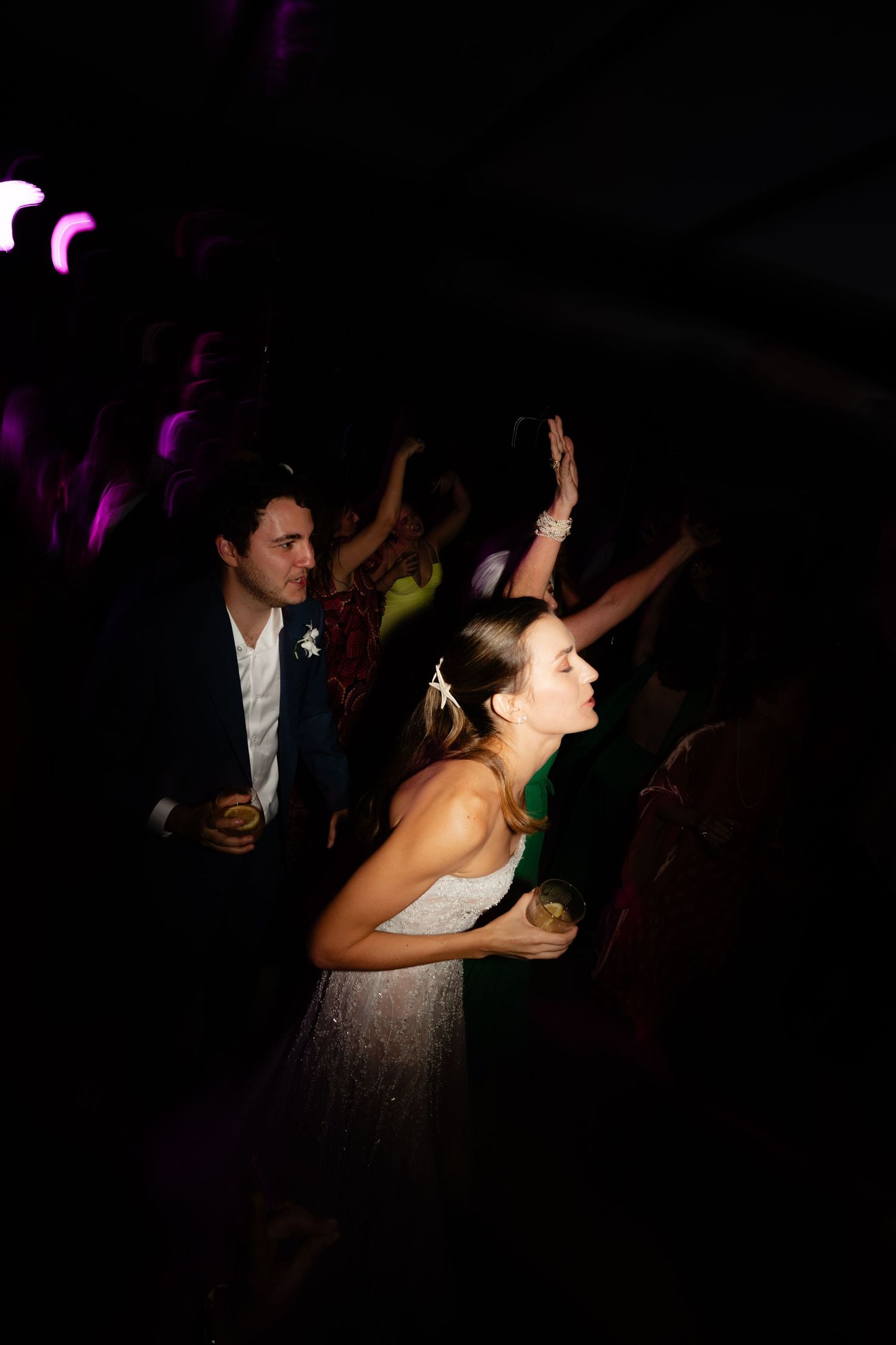 Bride dancing energetically in a white dress under dramatic purple lighting.