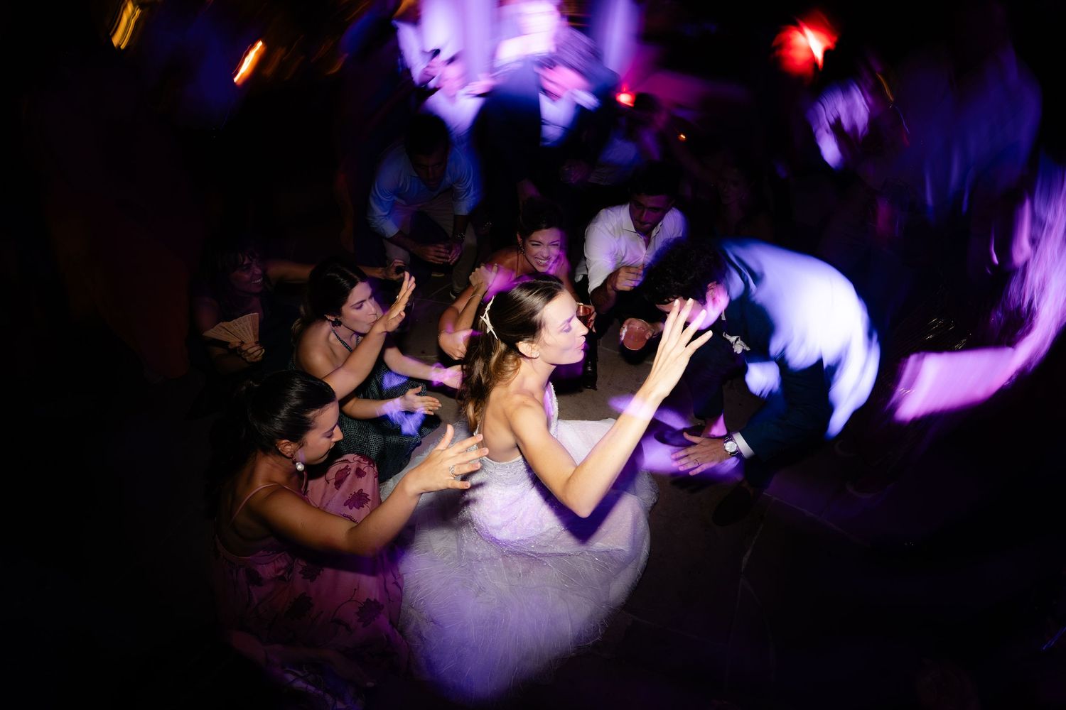 Crowd enjoying themselves on a dark dance floor illuminated by colorful club lighting.