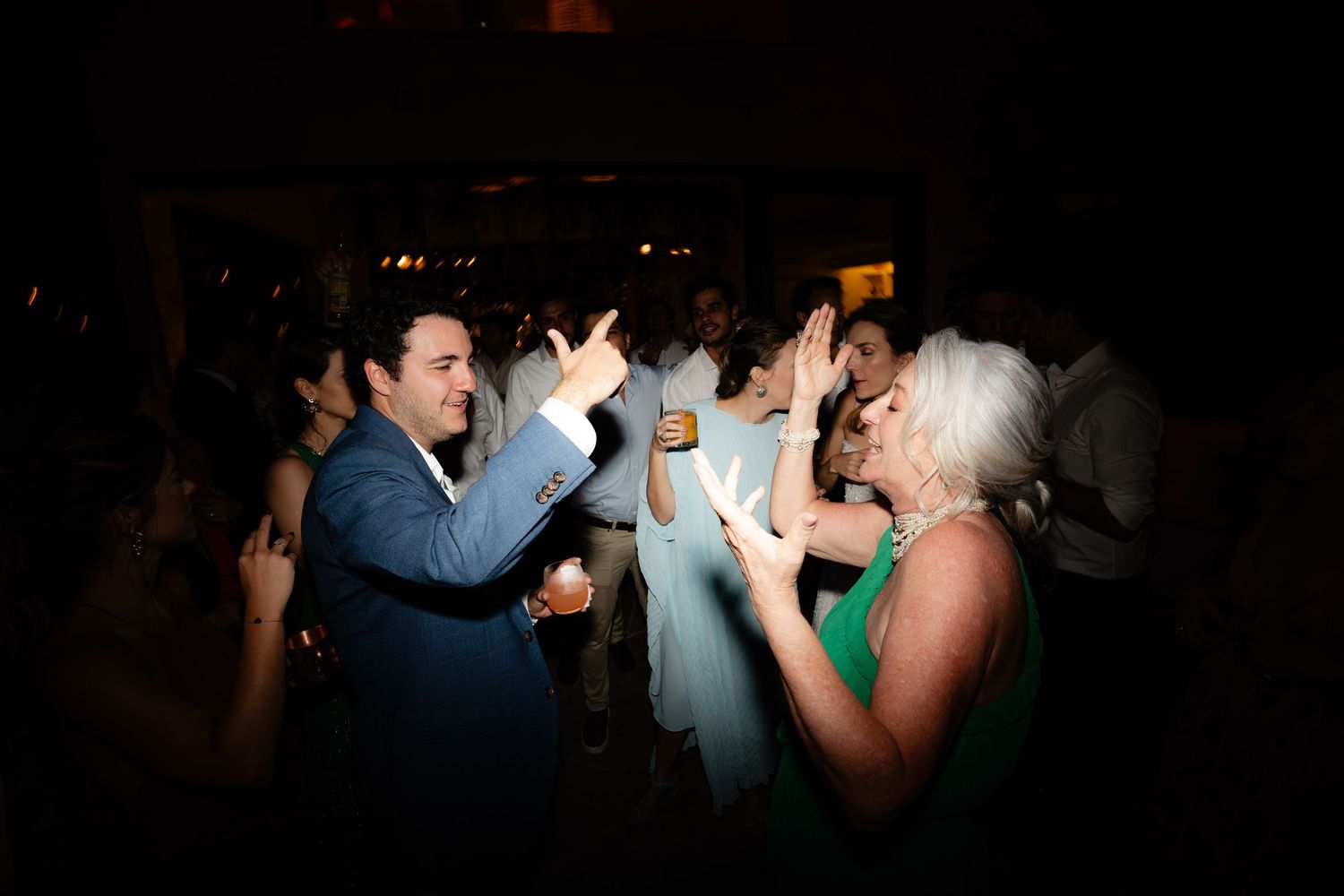 Group of celebrants dancing together under moody lighting at a festive event.
