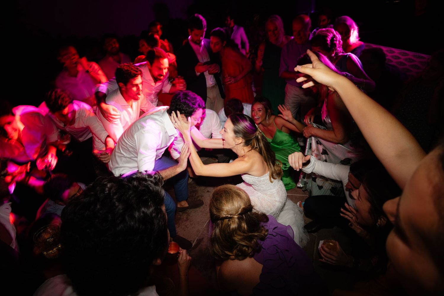Dance floor filled with party guests under purple and red mood lighting.
