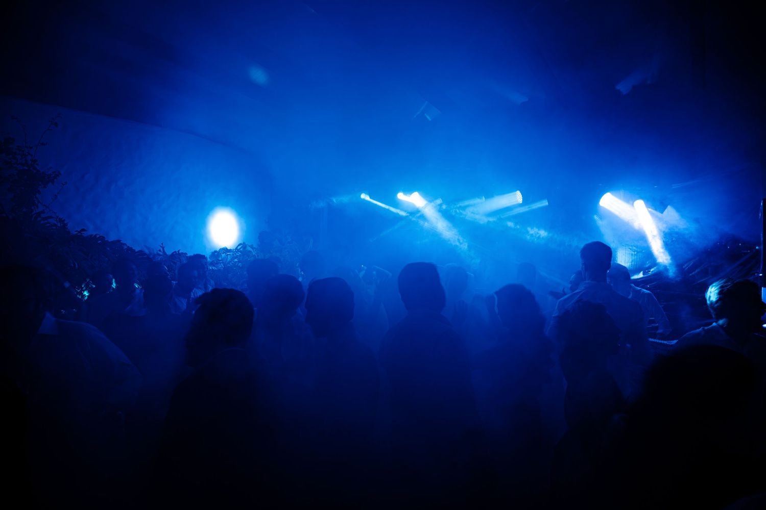 Blue concert lights illuminating a dark venue with silhouetted crowd in foreground.