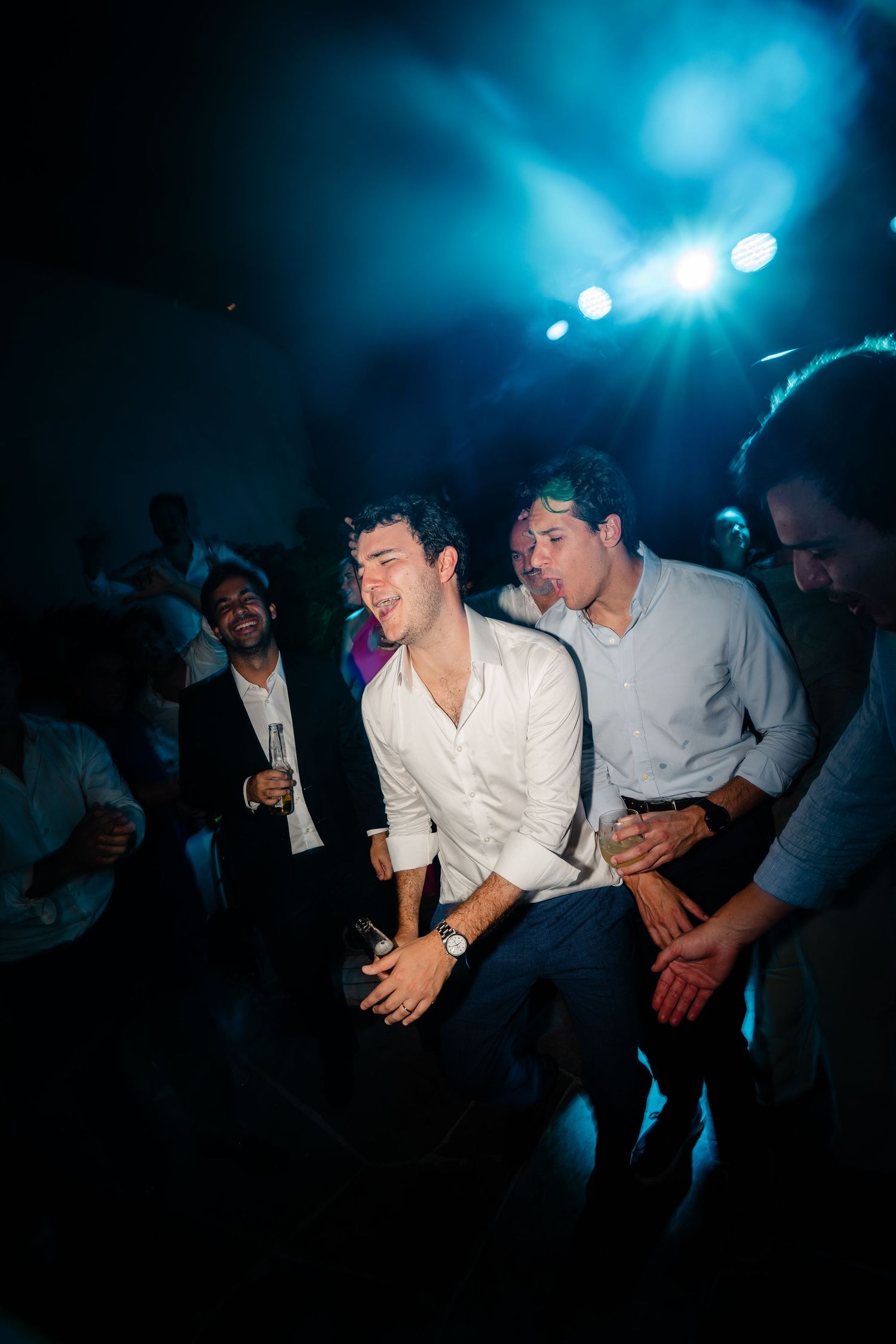 Group of party-goers dancing and laughing under blue lighting at a nightclub.