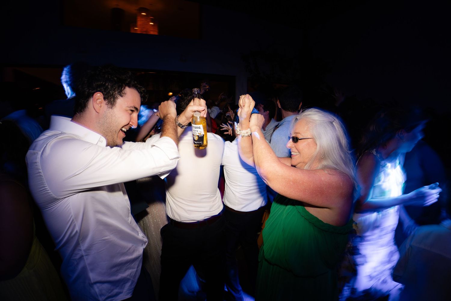 Group of party guests dancing and high-fiving on a dark dance floor with blue lighting.
