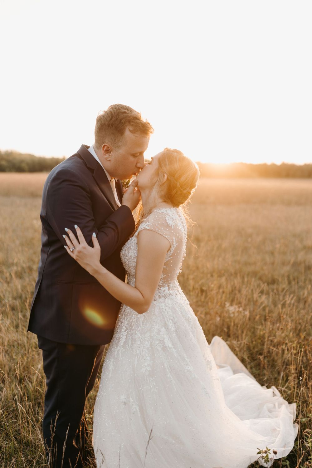 Bride and groom sharing romantic kiss in wheat field bathed in warm golden sunset light.