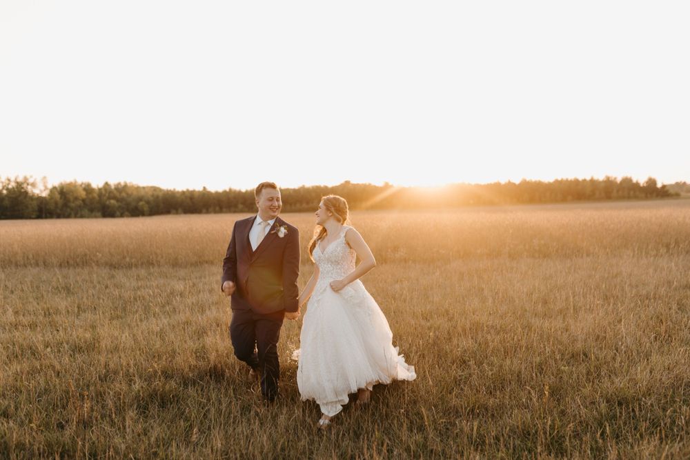 Smiling bride and groom standing together in glowing golden wheat field during sunset wedding portraits.