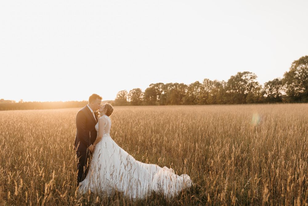 Couple shares a tender kiss in a glowing golden wheat field during magical sunset wedding portrait session.