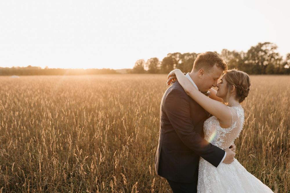 Bride and groom share a romantic almost-kiss in a breathtaking golden wheat field bathed in sunset light.