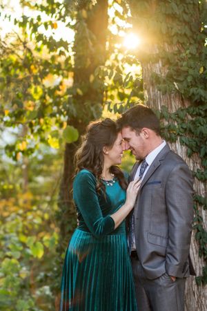 A couple shares a romantic moment outdoors, with golden sunlight filtering through lush green trees behind them.