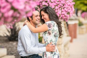 Couple embracing and laughing together outdoors with pink flowering trees in the background.