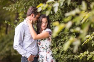 Couple shares an intimate moment surrounded by lush green leafy branches outdoors.