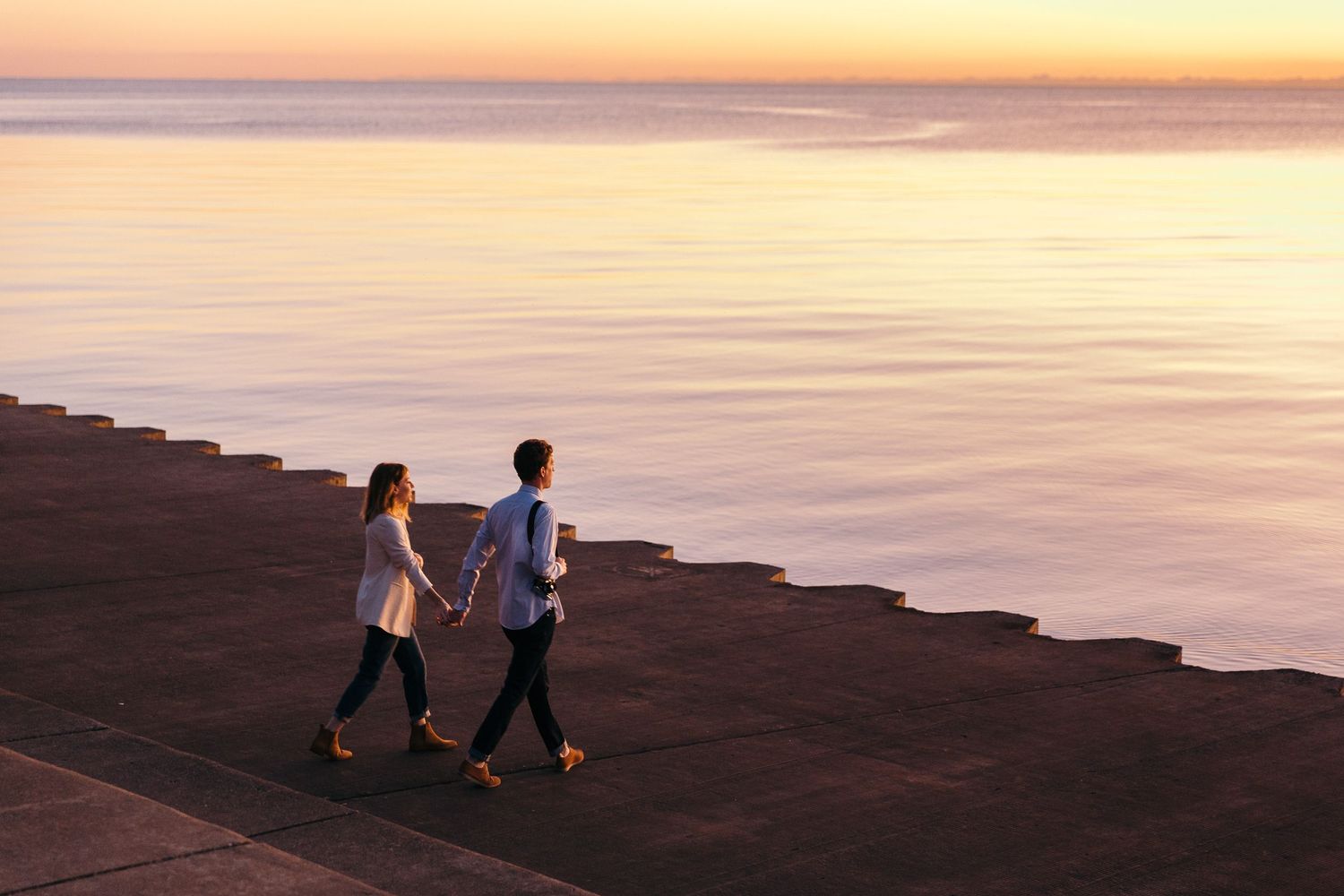 stylish couple in minimalist fall outfits hold hands in front of lake michigan at sunrise