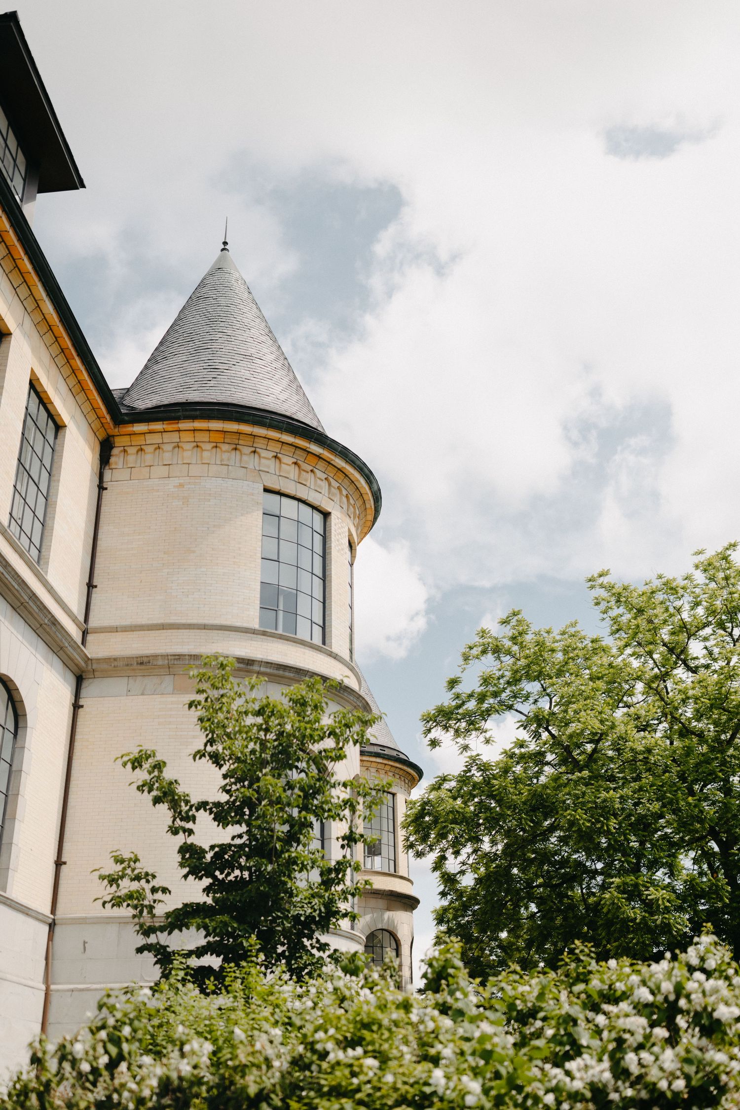 Elegant white stone castle tower with conical turret and arched windows against a cloudy sky.