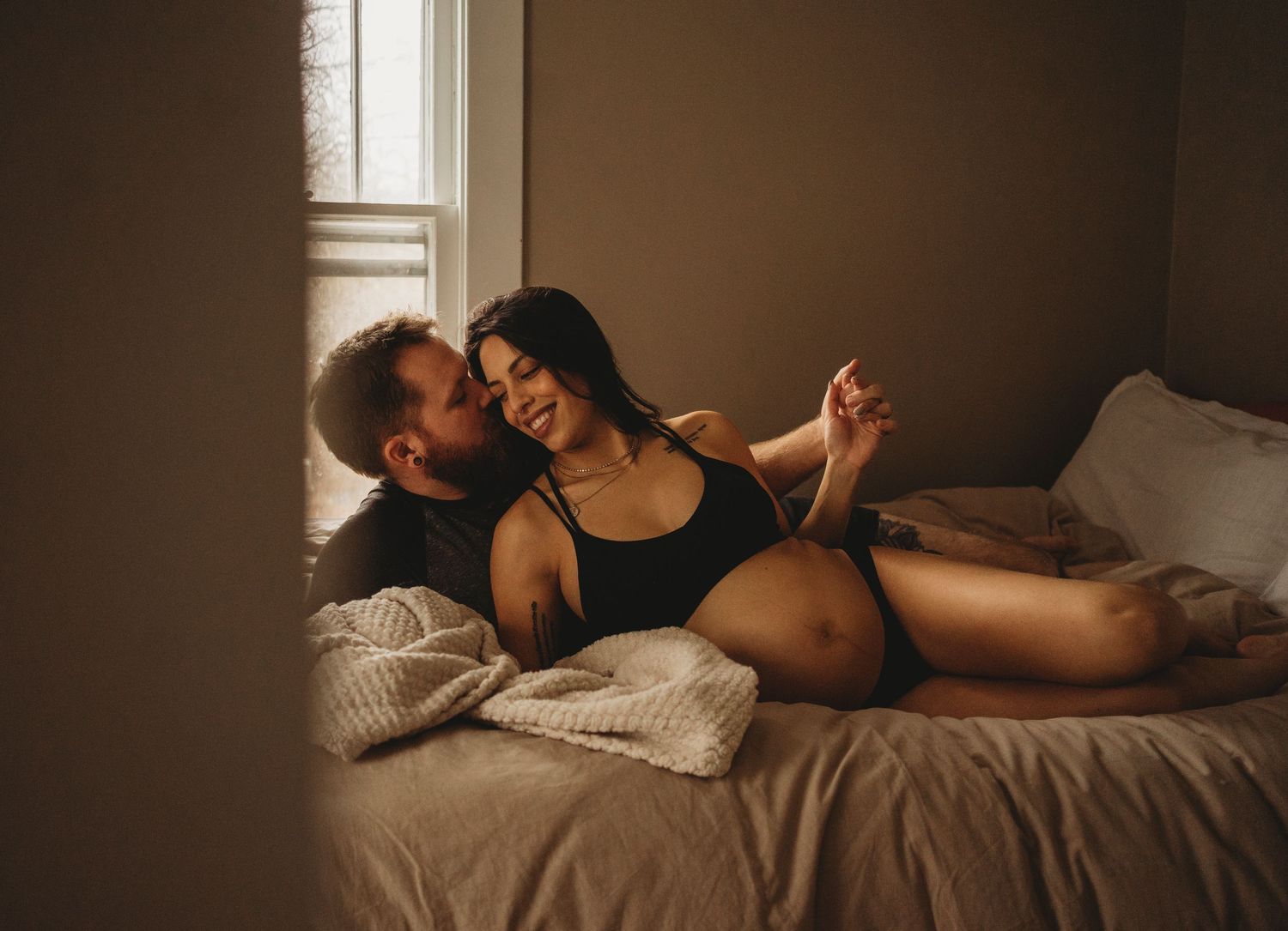 Romantic couple embracing on bed in moody lighting and warm tones.