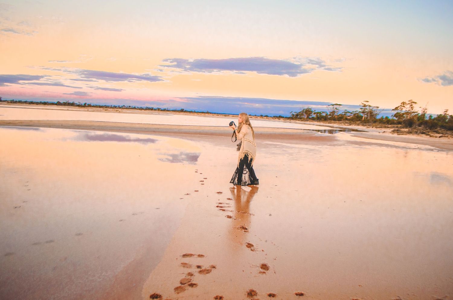 Couple walking on beach at sunset leaving footprints in wet sand.