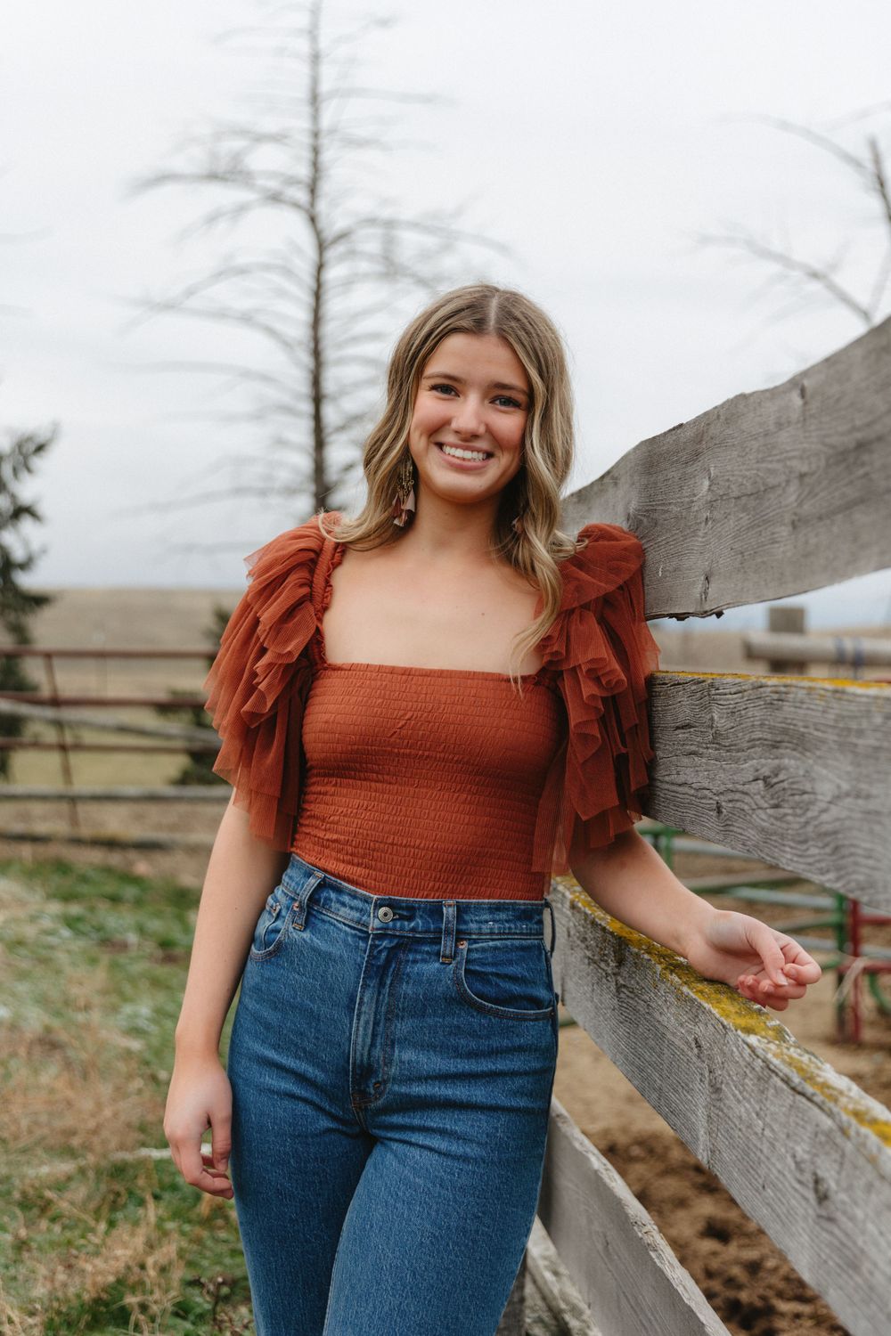 A casual outdoor portrait of a young woman leaning against a wooden fence.