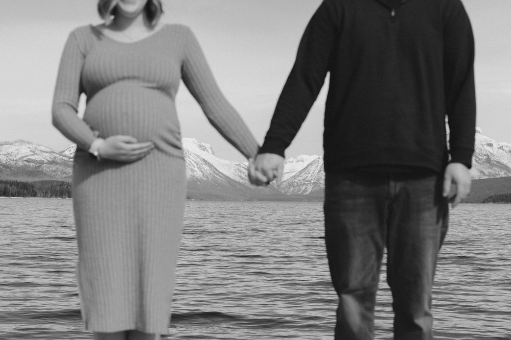 A silhouetted couple holds hands by a lake with mountains in the background.