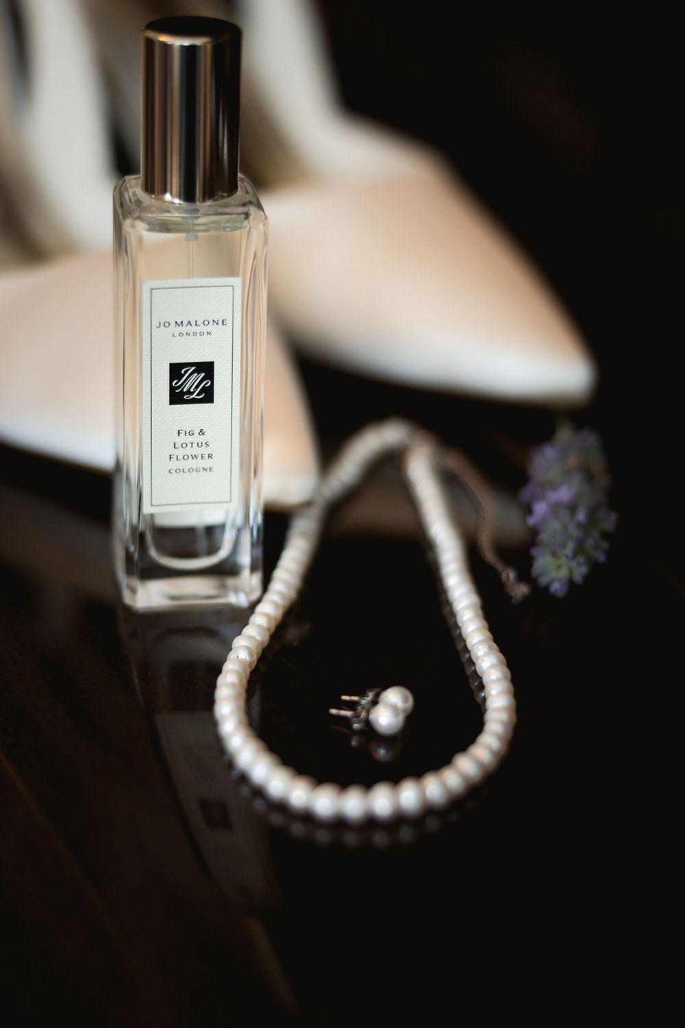 Elegant perfume bottle with pearl necklace and floral accents on dark surface.