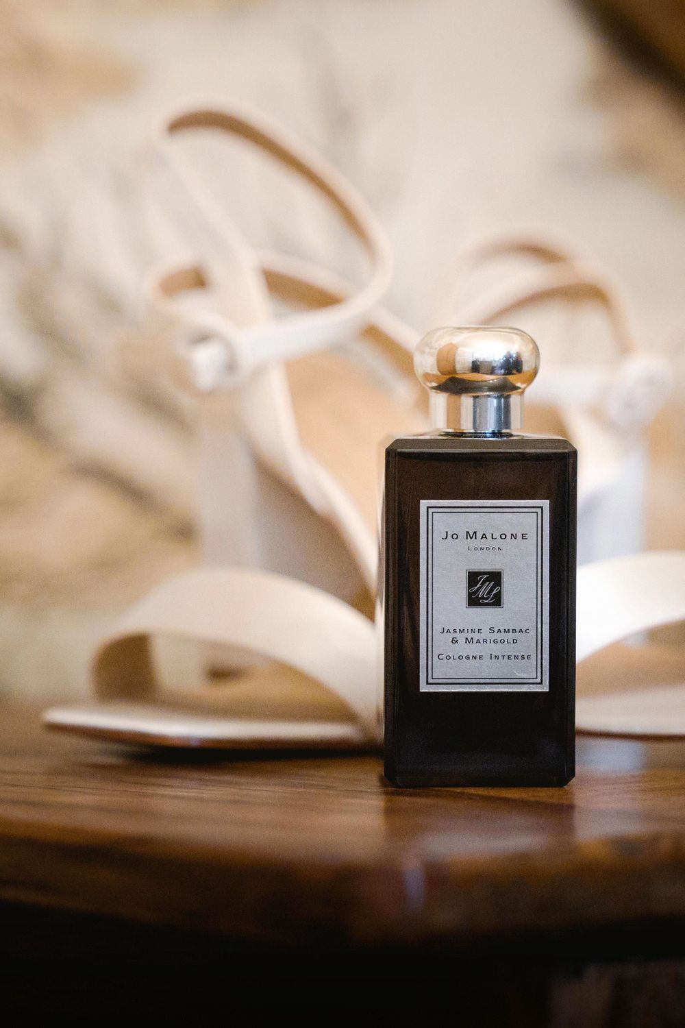 A Jo Malone perfume bottle elegantly positioned next to cream-colored wedding shoes.
