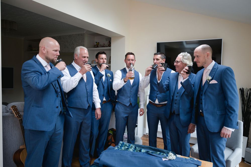 Groomsmen in coordinated blue suits gather together for a candid moment at a wedding.