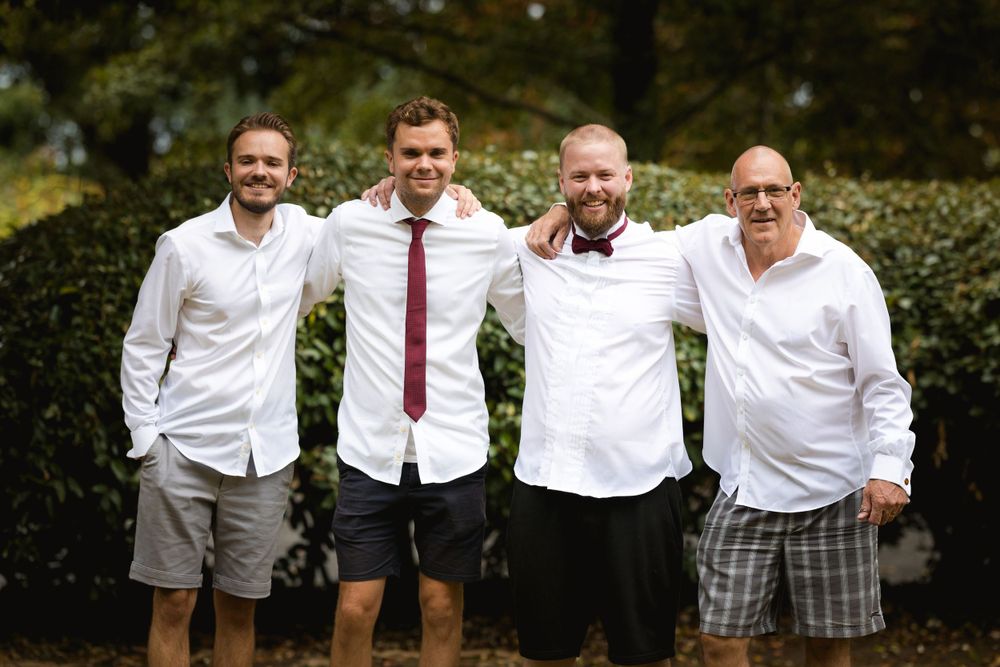 Group of four men in white shirts posing casually outdoors.
